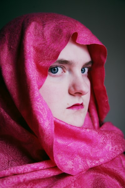 一个戴着粉色头巾的女人，用紫色的纺织品遮住她的脸